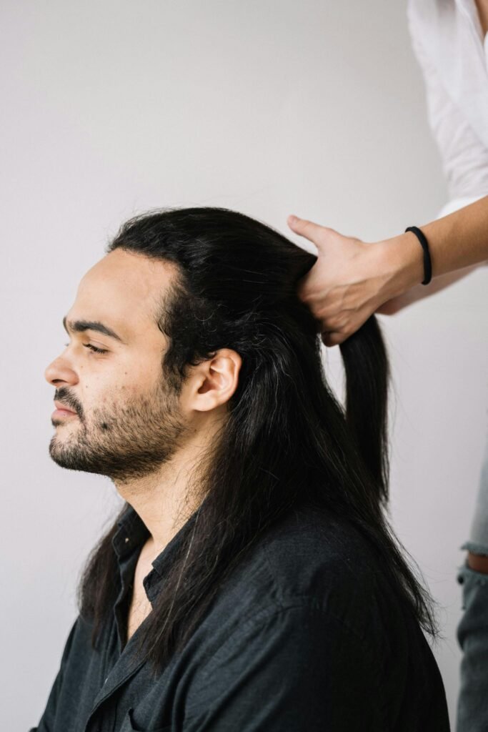 Profile of a man with long hair being styled into a ponytail.